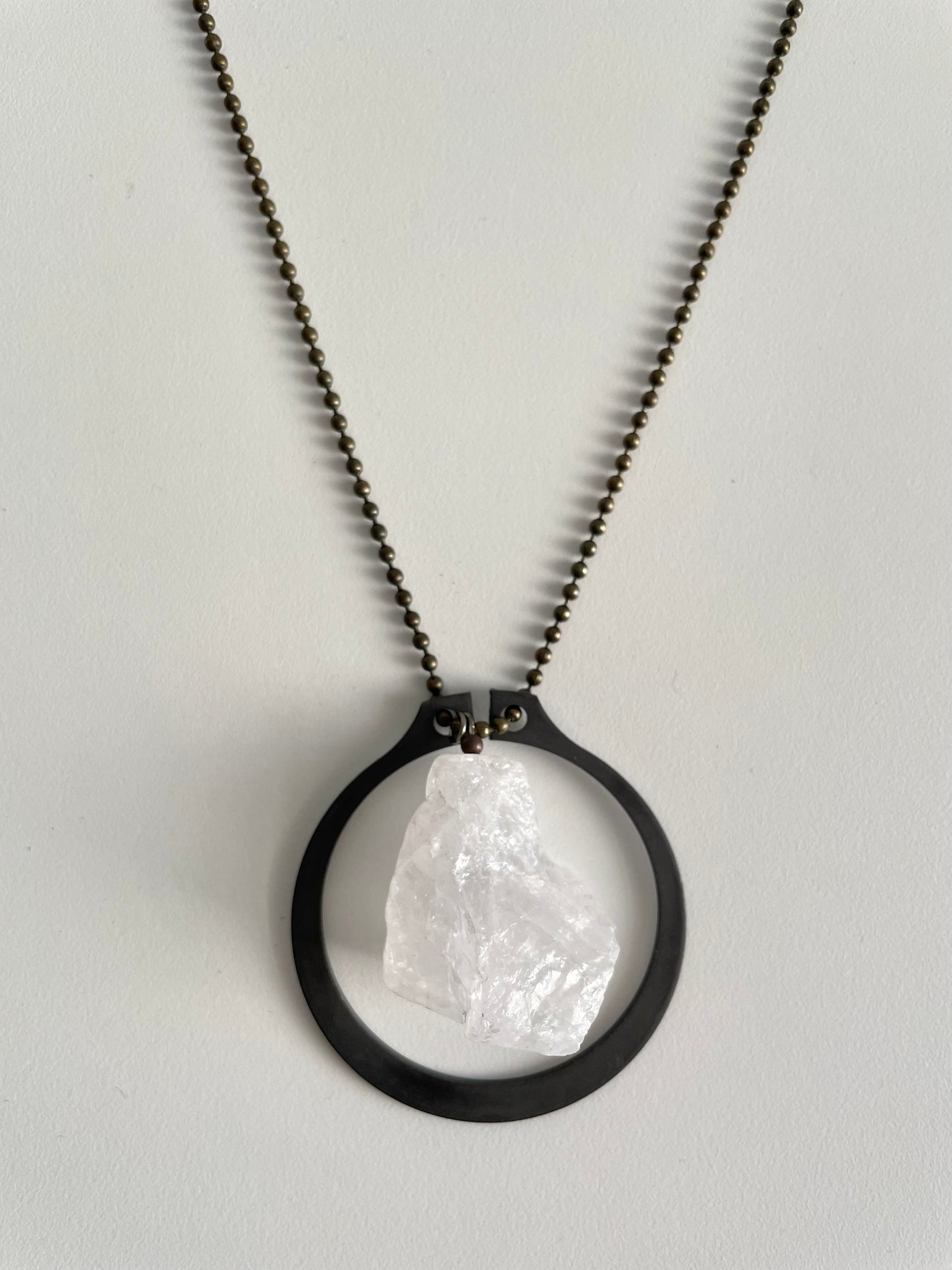 A statement neckalce with a large quartz crystal within a matte dark brown iron frame